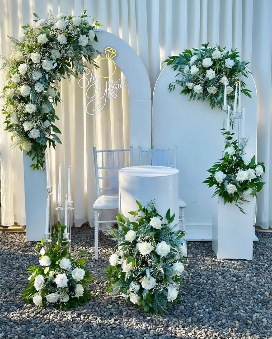 White arch with greenery and crystal chairs